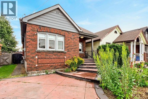 Brick exterior with a gabled roofline, stone window sills, and a concrete driveway - 136 Weir Street N, Hamilton, ON 