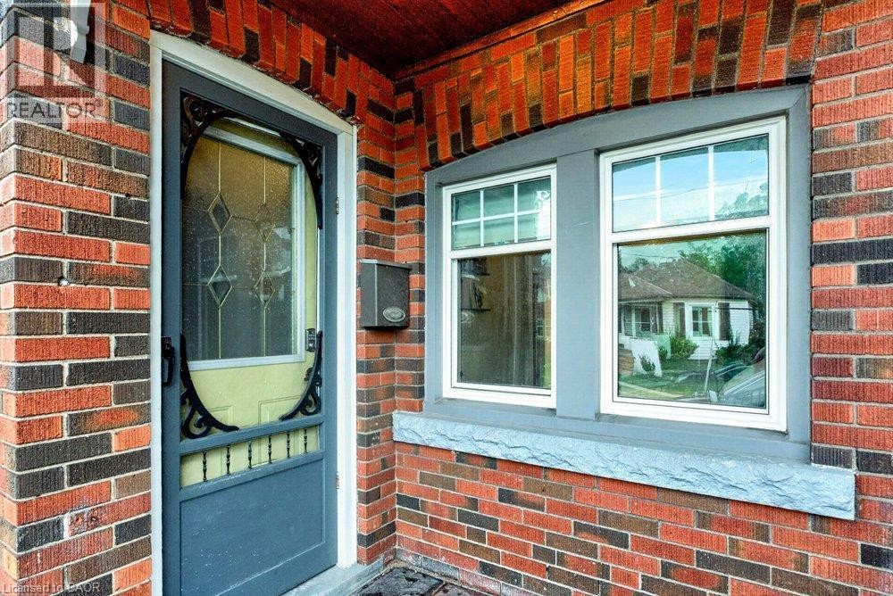 Brick exterior with a decorative screen door, double-hung windows, and a stone window sill - 136 Weir Street N, Hamilton, ON