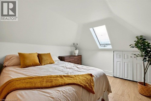 Angled ceiling lines with a skylight, light laminate flooring, and white bifold closet doors - 136 Weir Street N, Hamilton, ON 