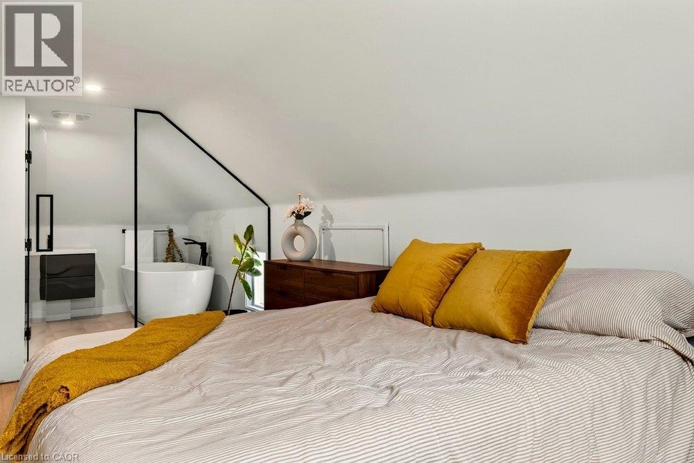 Sloped ceiling design with recessed lighting, freestanding bathtub, wall-mounted vanity, and laminate flooring - 136 Weir Street N, Hamilton, ON