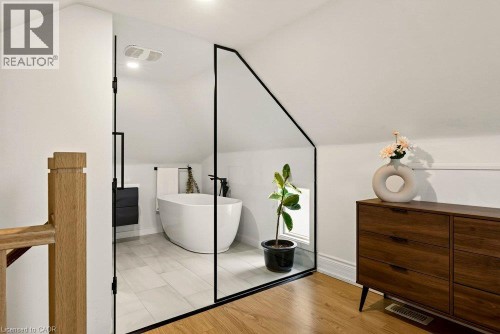 Modern bathroom featuring a freestanding soaking tub, tiled flooring, and a sleek black-framed glass enclosure - 136 Weir Street N, Hamilton, ON 