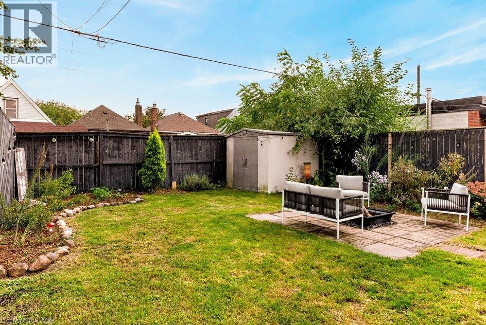 Expansive backyard featuring a lush lawn, a stone-edged garden bed, a paver patio, a storage shed, and a privacy fence - 136 Weir Street N, Hamilton, ON