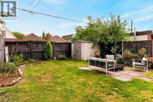Expansive backyard featuring a lush lawn, a stone-edged garden bed, a paver patio, a storage shed, and a privacy fence - 136 Weir Street N, Hamilton, ON 