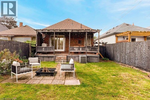 Expansive backyard featuring a manicured lawn, brick paver patio, wood deck, pergola, and brick exterior - 136 Weir Street N, Hamilton, ON 