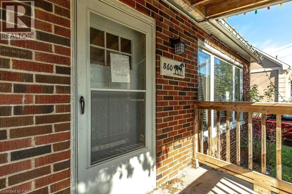 Brick exterior with a storm door, wood railing, and an exterior light fixture - 860 Garth Street, Hamilton, ON