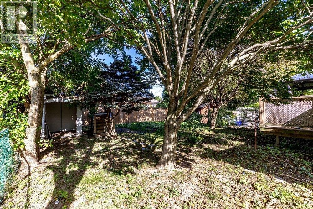 Expansive backyard featuring mature trees, a wooden fence, and a wooden deck with lattice detailing - 860 Garth Street, Hamilton, ON