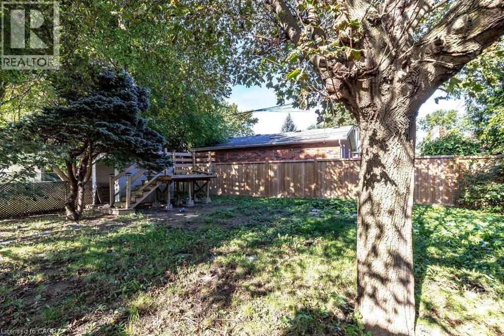 Expansive backyard featuring mature trees, a wooden privacy fence, and an elevated wooden deck with stairs - 860 Garth Street, Hamilton, ON