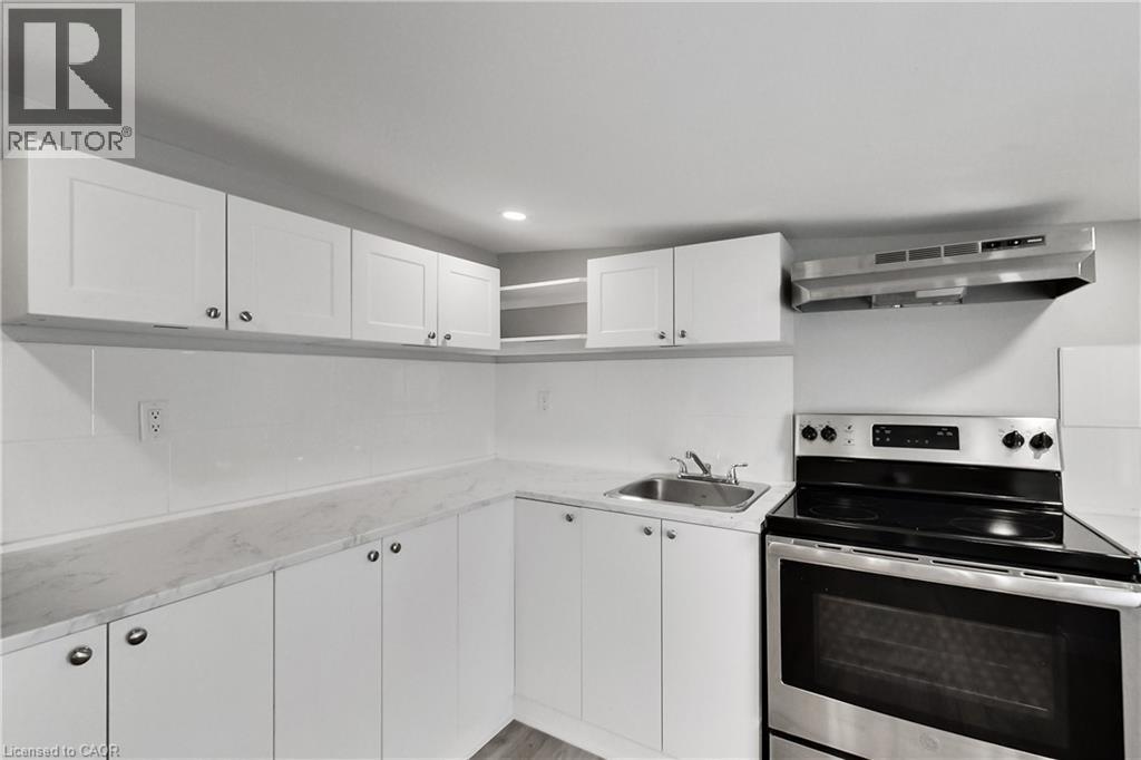 Contemporary kitchen featuring white cabinetry, light-toned countertops, a stainless steel range, and a coordinating range hood - 229 Parkdale Avenue N, Hamilton, ON