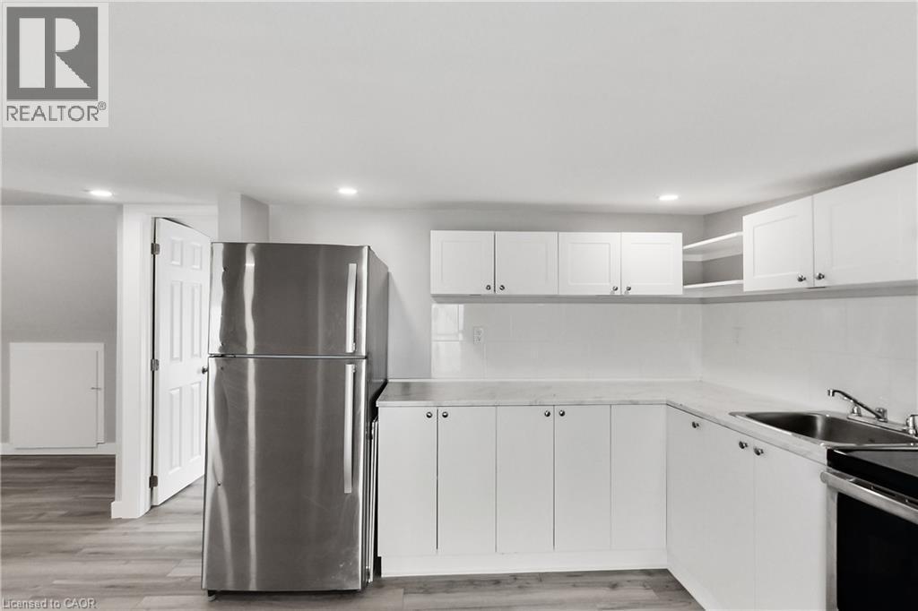 Stainless steel refrigerator, white cabinetry, integrated sink, overhead recessed lighting, and wood-finish flooring - 229 Parkdale Avenue N, Hamilton, ON