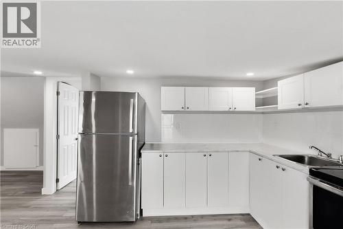 Stainless steel refrigerator, white cabinetry, integrated sink, overhead recessed lighting, and wood-finish flooring - 229 Parkdale Avenue N, Hamilton, ON 