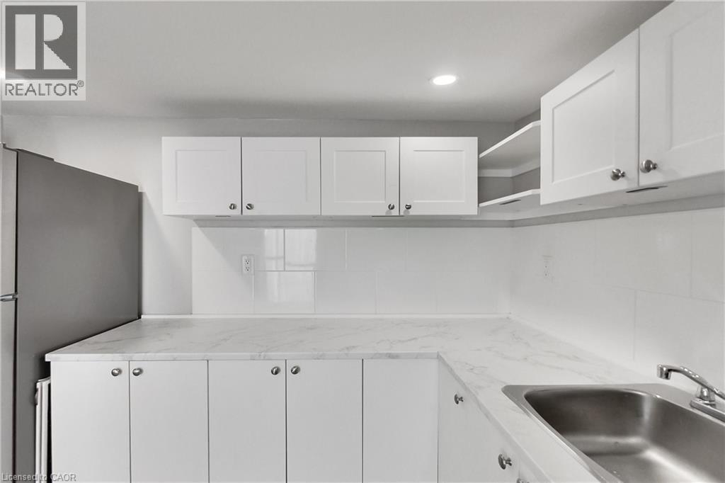 White shaker-style cabinetry with satin nickel hardware, stainless steel sink, tile backsplash, and recessed lighting - 229 Parkdale Avenue N, Hamilton, ON