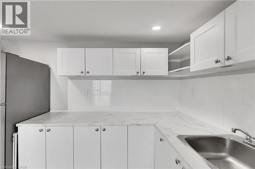 White shaker-style cabinetry with satin nickel hardware, stainless steel sink, tile backsplash, and recessed lighting - 229 Parkdale Avenue N, Hamilton, ON 