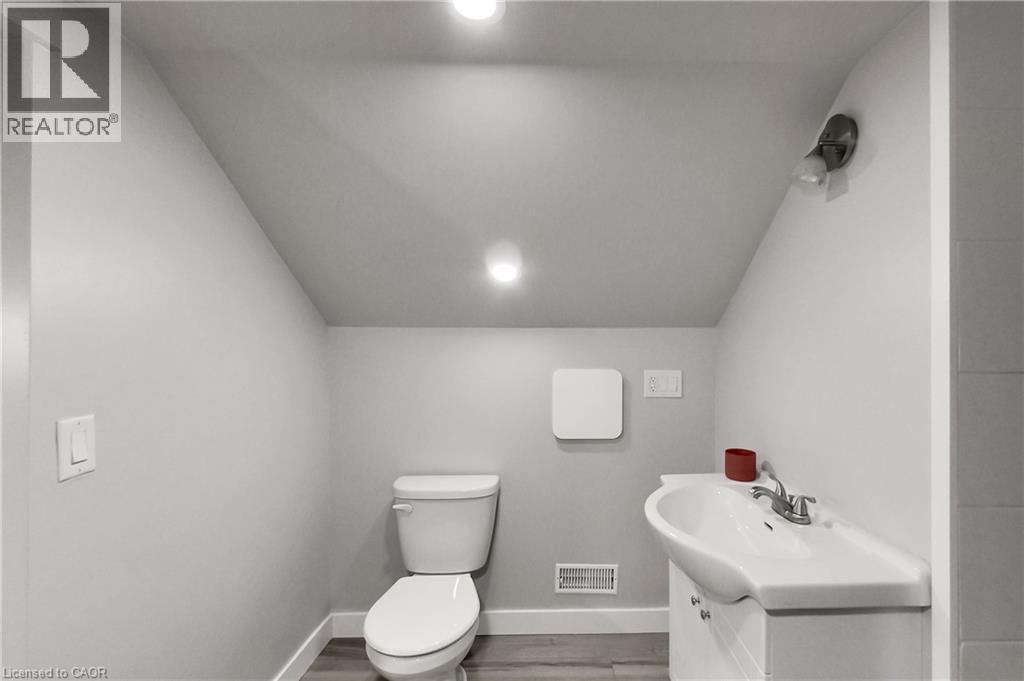 Recessed ceiling lighting, angled ceiling, white toilet, wall-mounted vanity light, wood-finish flooring - 229 Parkdale Avenue N, Hamilton, ON