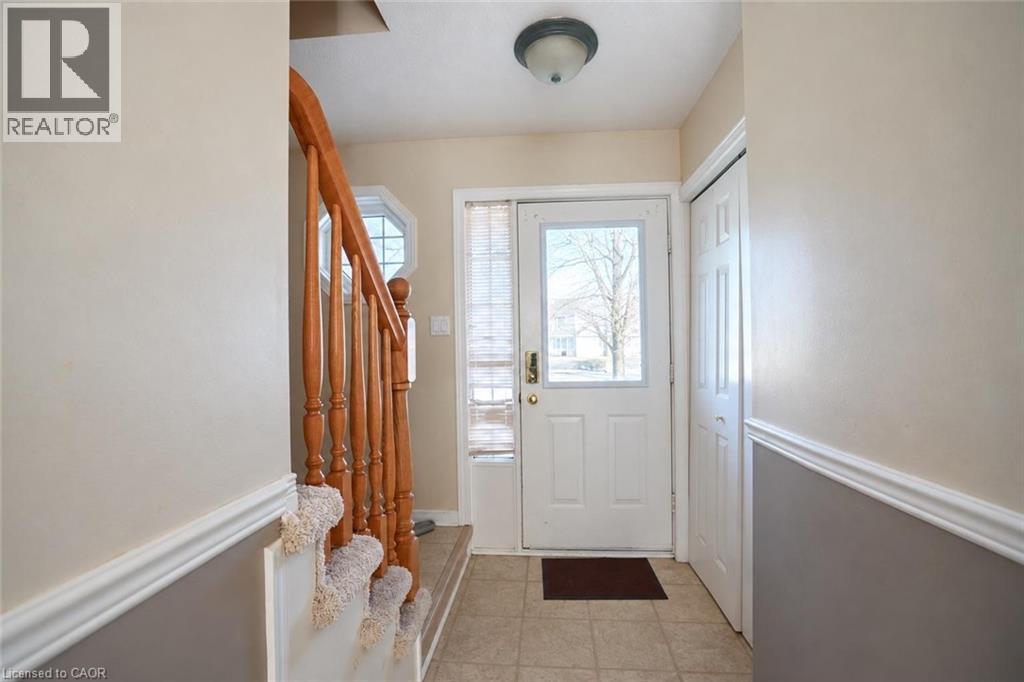 Tiled flooring entry with a white paneled door, natural wood staircase, and an octagonal window - 95 Resurrection Drive, Kitchener, ON