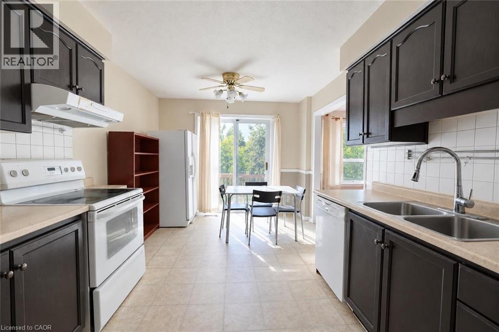 Kitchen featuring dark wood cabinetry, light-toned countertops, white tile backsplash, and a dual basin stainless steel sink with a pull-down faucet - 95 Resurrection Drive, Kitchener, ON