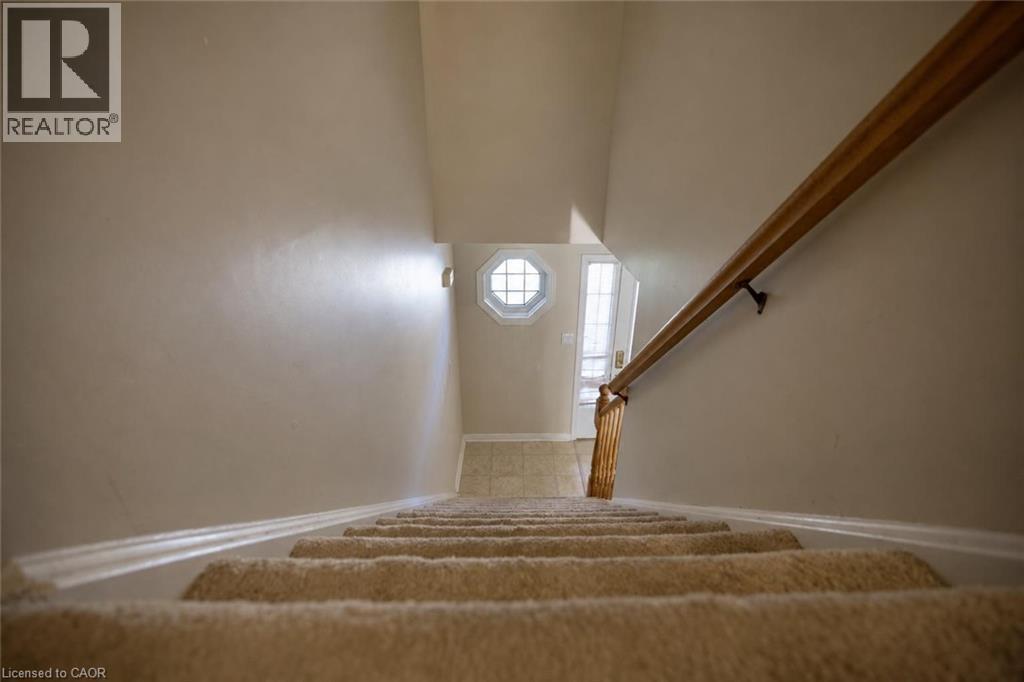 Carpeted staircase with wood handrail, leading to a tiled entry with a decorative octagonal window - 95 Resurrection Drive, Kitchener, ON