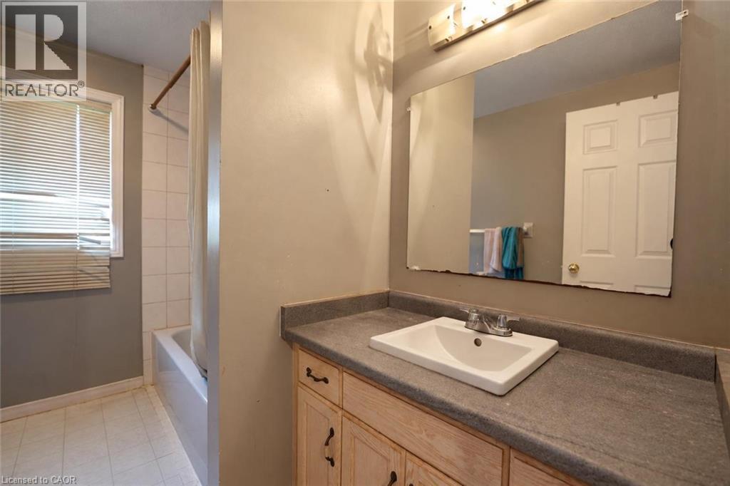 Bathroom featuring a single vanity with an integrated sink, a built-in mirror, and a tub with a shower enclosure - 95 Resurrection Drive, Kitchener, ON