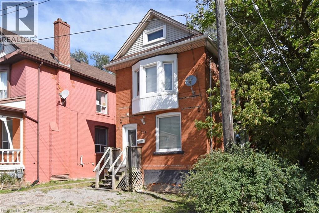 Brick exterior featuring a bay window with white trim, a gabled roofline, and a prominent front entrance - 734 King Street W, Hamilton, ON
