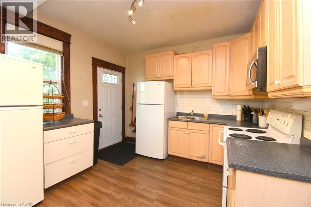 Wood-finish flooring with light-toned cabinetry, a white subway tile backsplash, and dark countertops - 734 King Street W, Hamilton, ON