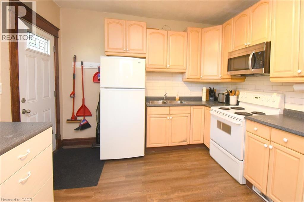 Kitchen featuring wood-finish flooring, light cabinetry, dark countertops, a white subway tile backsplash, and stainless steel microwave - 734 King Street W, Hamilton, ON