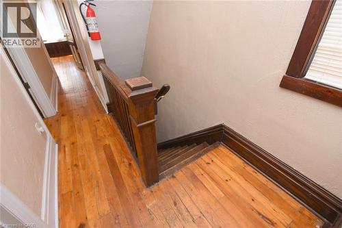 Hardwood flooring extending through the hallway, rich wood-toned staircase with balusters, and a window with wood trim - 734 King Street W, Hamilton, ON 