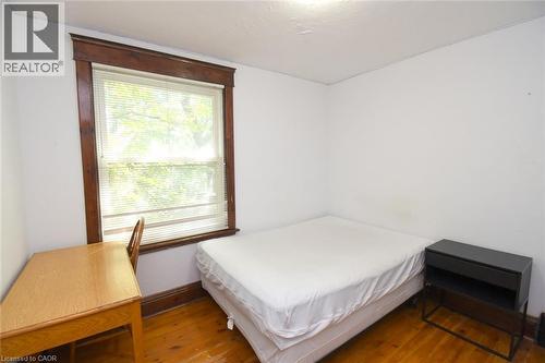 Bright room featuring wood-finish flooring, a window with wood trim, and white walls - 734 King Street W, Hamilton, ON 