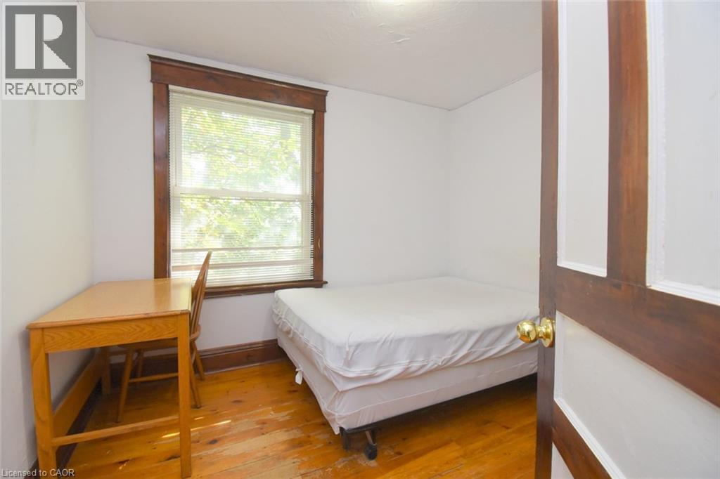 Hardwood flooring, window with blinds, white walls, and a paneled interior door with brass hardware - 734 King Street W, Hamilton, ON