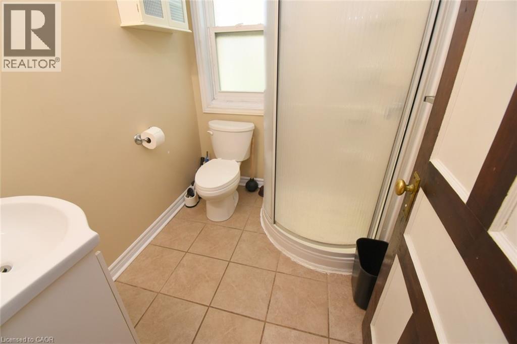 Bathroom featuring a corner shower enclosure, window, pedestal sink, and tiled flooring - 734 King Street W, Hamilton, ON