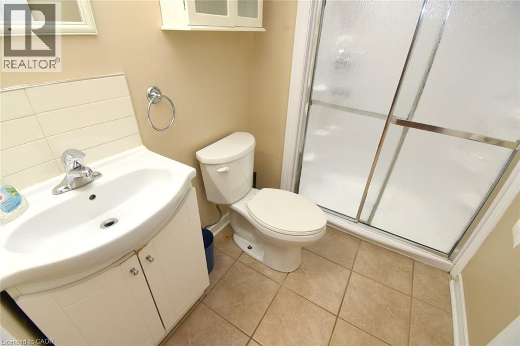 Shower enclosure with sliding frosted glass doors, white vanity with integrated sink, chrome faucet, wall-mounted storage cabinet, and tile flooring - 734 King Street W, Hamilton, ON