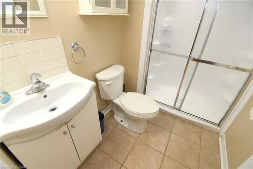 Shower enclosure with sliding frosted glass doors, white vanity with integrated sink, chrome faucet, wall-mounted storage cabinet, and tile flooring - 734 King Street W, Hamilton, ON 