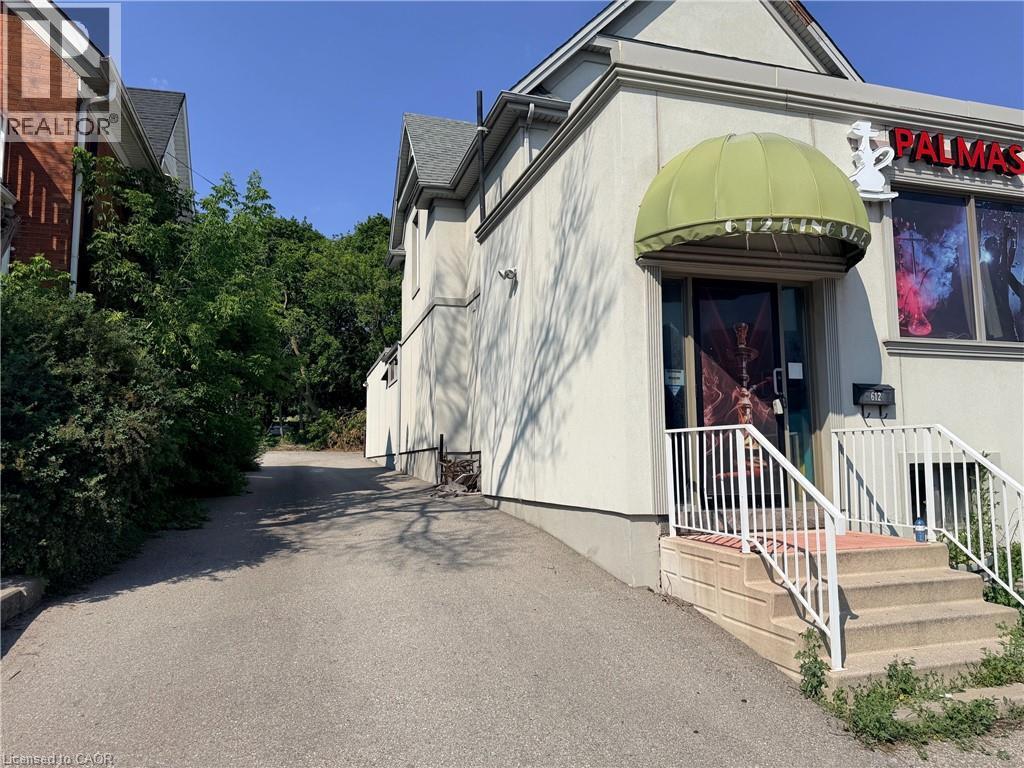 Building exterior featuring a light-colored stucco finish, a green fabric awning, and a prominent entrance with concrete steps and white railings - 612 King Street E, Kitchener, ON