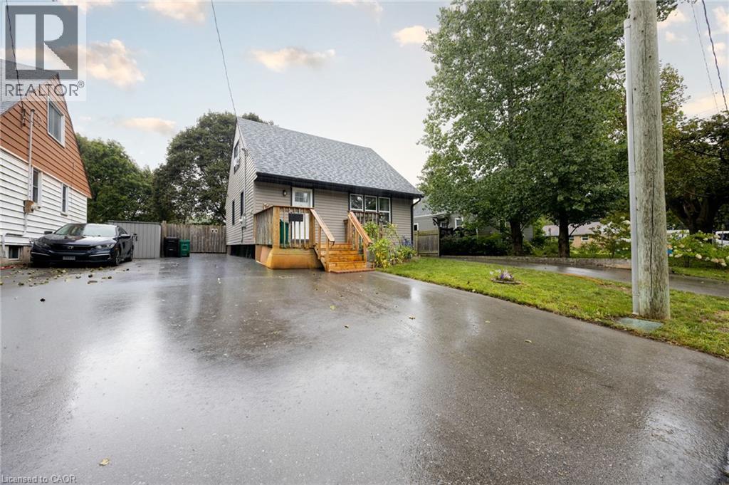 Asphalt driveway with a fenced property line, wood siding, and mature trees - 102 Stewart Avenue, Cambridge, ON