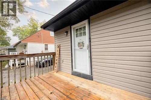 Wood deck with railing, light-colored horizontal siding, exterior door with glass panes, black roofline trim, and an exterior wall lantern - 102 Stewart Avenue, Cambridge, ON 