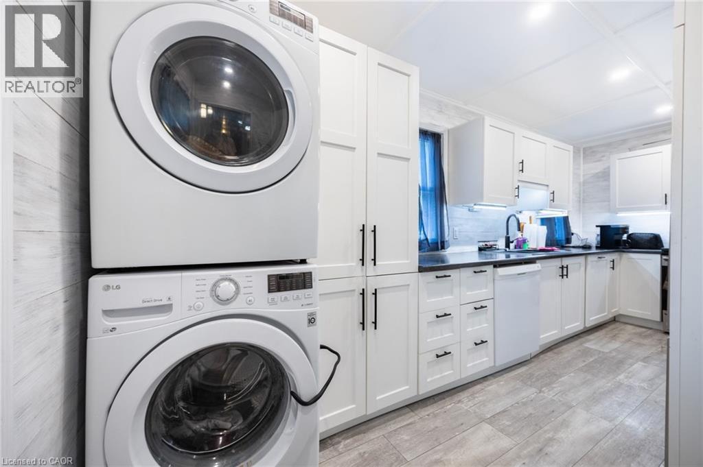 White shaker-style cabinetry with matte black hardware, dark countertops, tile backsplash, wood-finish flooring, and a stacked washer and dryer unit - 102 Stewart Avenue, Cambridge, ON