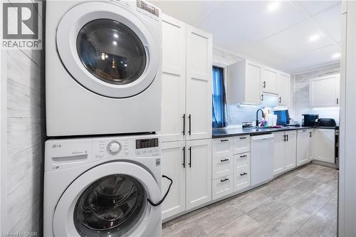 White shaker-style cabinetry with matte black hardware, dark countertops, tile backsplash, wood-finish flooring, and a stacked washer and dryer unit - 102 Stewart Avenue, Cambridge, ON 
