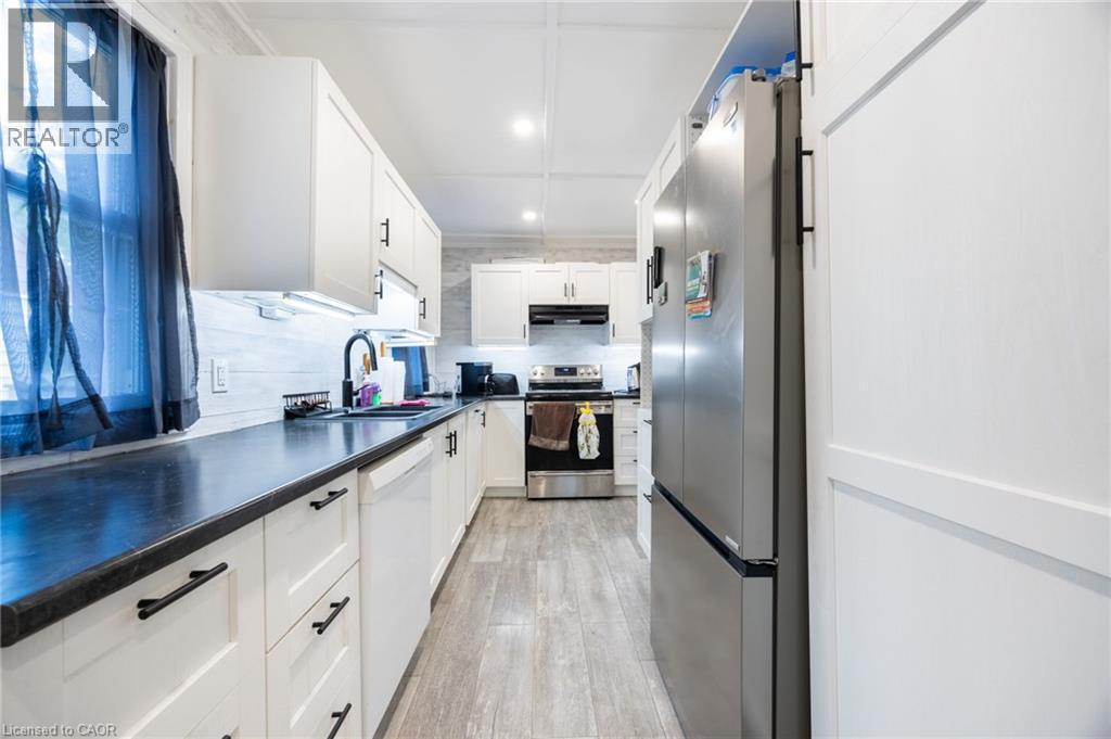 Modern kitchen featuring white cabinetry with black hardware, dark countertops, a stainless steel refrigerator, and wood-finish flooring - 102 Stewart Avenue, Cambridge, ON