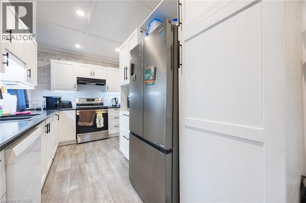 Kitchen featuring white shaker-style cabinetry, dark countertops, stainless steel appliances, and wood-finish flooring - 102 Stewart Avenue, Cambridge, ON