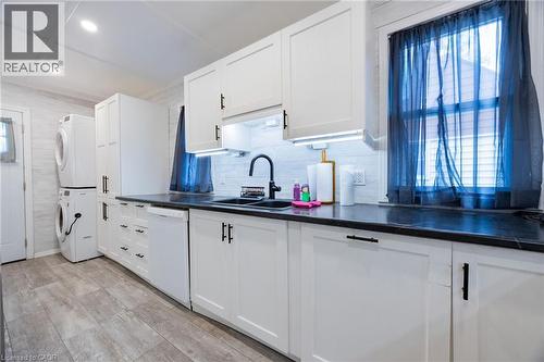 White shaker-style cabinetry with black hardware, dark countertops, white tile backsplash, wood-finish flooring, and recessed ceiling lighting - 102 Stewart Avenue, Cambridge, ON 