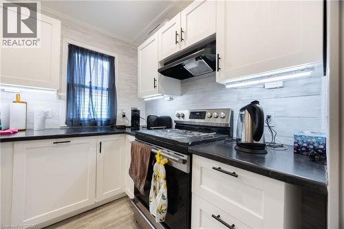 White shaker-style cabinetry with black hardware, dark countertops, stainless steel range with overhead ventilation, and under-cabinet lighting - 102 Stewart Avenue, Cambridge, ON 