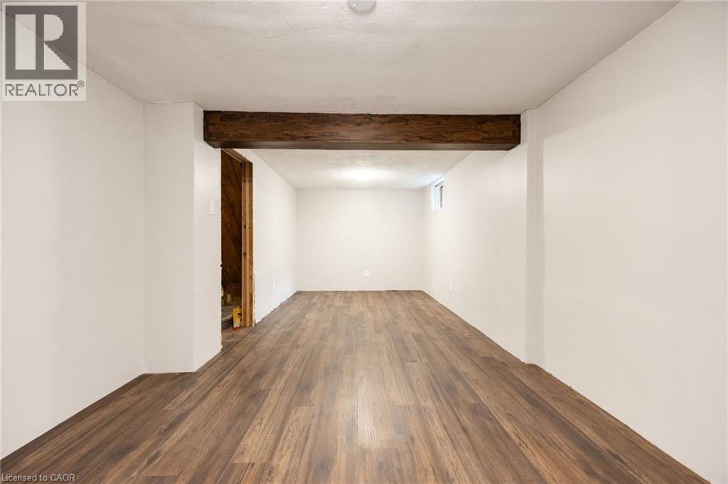 Spacious room featuring wood-finish flooring, white walls, exposed wood beam, and a single window - 102 Stewart Avenue, Cambridge, ON