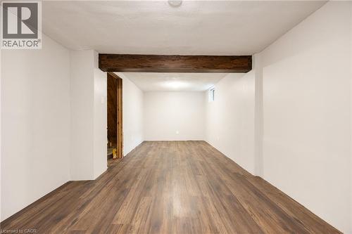 Spacious room featuring wood-finish flooring, white walls, exposed wood beam, and a single window - 102 Stewart Avenue, Cambridge, ON 