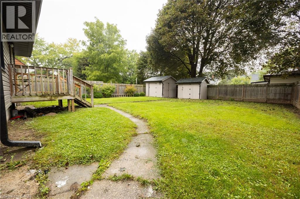 Expansive fenced backyard featuring a wood deck, concrete pathway, two storage sheds, and mature trees - 102 Stewart Avenue, Cambridge, ON