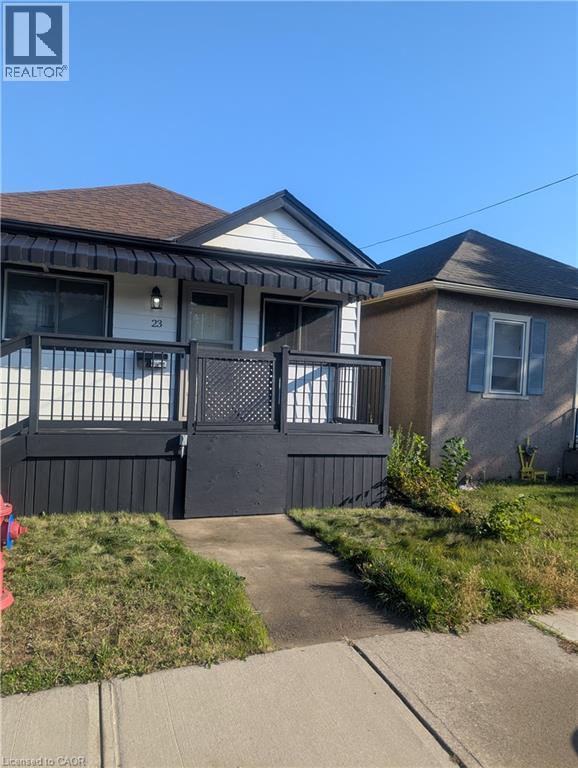 Exterior featuring white horizontal siding, a raised deck with black metal railing, an integrated metal awning, and a gabled roof - 23 Harrison Avenue, Hamilton, ON