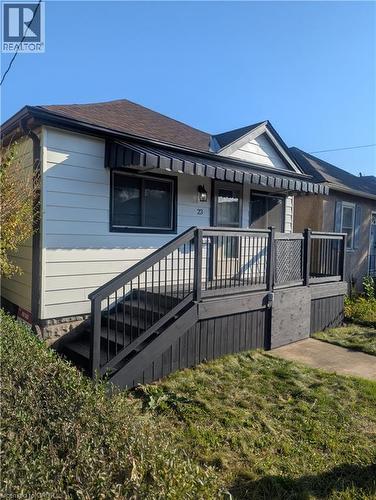 Exterior featuring horizontal siding, a gabled roofline, a raised wooden deck with dark-finish metal railings, and a protective window awning - 23 Harrison Avenue, Hamilton, ON 