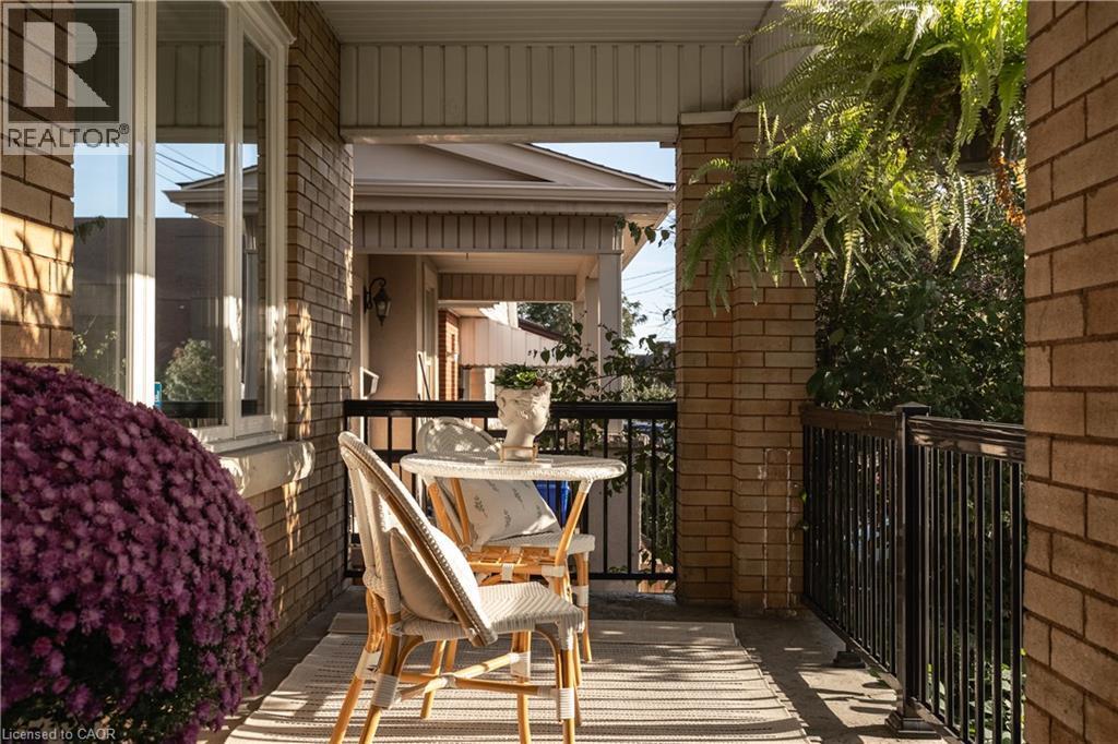 Covered front porch with brick columns, white window trim, and black metal railings - 50 Norway Avenue, Hamilton, ON