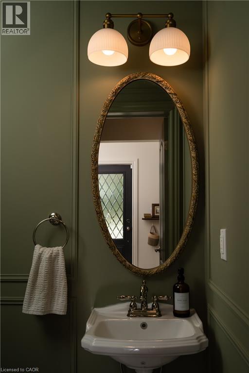 Pedestal sink with polished chrome fixtures, an oval framed mirror, and a two-light vanity fixture - 50 Norway Avenue, Hamilton, ON