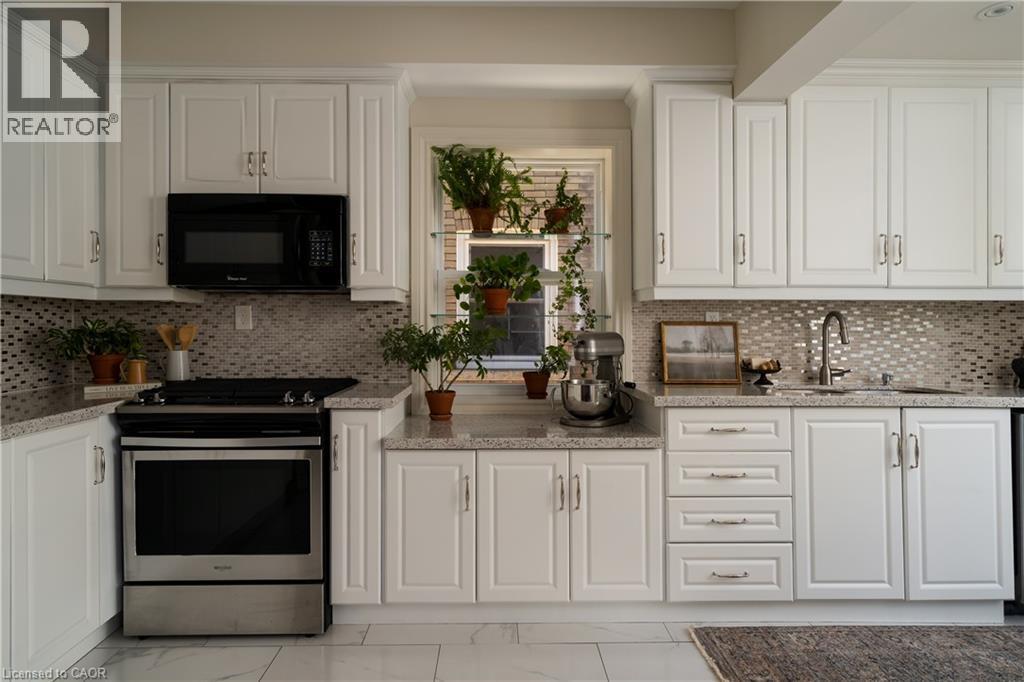 White cabinetry, patterned tile backsplash, stainless steel range, stainless steel microwave, and light-toned countertops - 50 Norway Avenue, Hamilton, ON