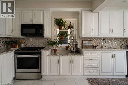 White cabinetry, patterned tile backsplash, stainless steel range, stainless steel microwave, and light-toned countertops - 50 Norway Avenue, Hamilton, ON 