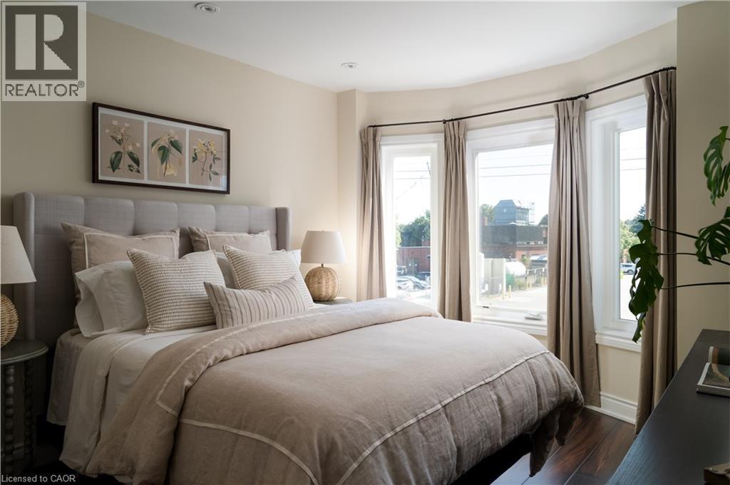 Bay window with three large windows, recessed ceiling lighting, light-toned wall paint, dark wood-finish flooring, and a fabric-upholstered headboard - 50 Norway Avenue, Hamilton, ON
