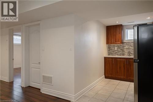 Compact kitchenette featuring wood-finish cabinetry, a single basin sink, and mosaic tile backsplash - 50 Norway Avenue, Hamilton, ON 